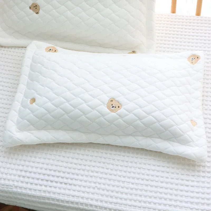 A white quilted soft cooling pillow for newborns resting on a white textured surface.