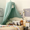 A princess hanging bed canopy with light green fabric and white bedding is shown in a bright room.