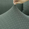 A close-up of a dark gray woven fabric sofa cover with an intricate geometric pattern being touched by a hand.