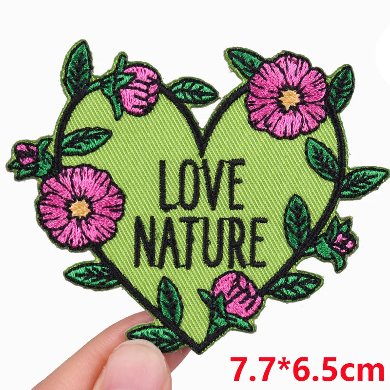 A green heart shaped embroidered patch with pink flowers and green leaves.