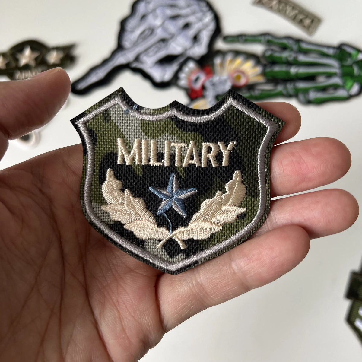A hand holds a military themed embroidered patch featuring a star and leaves on a dark green fabric.