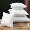 A stack of three white polyester cushion inserts for throw pillows resting on a beige fabric.