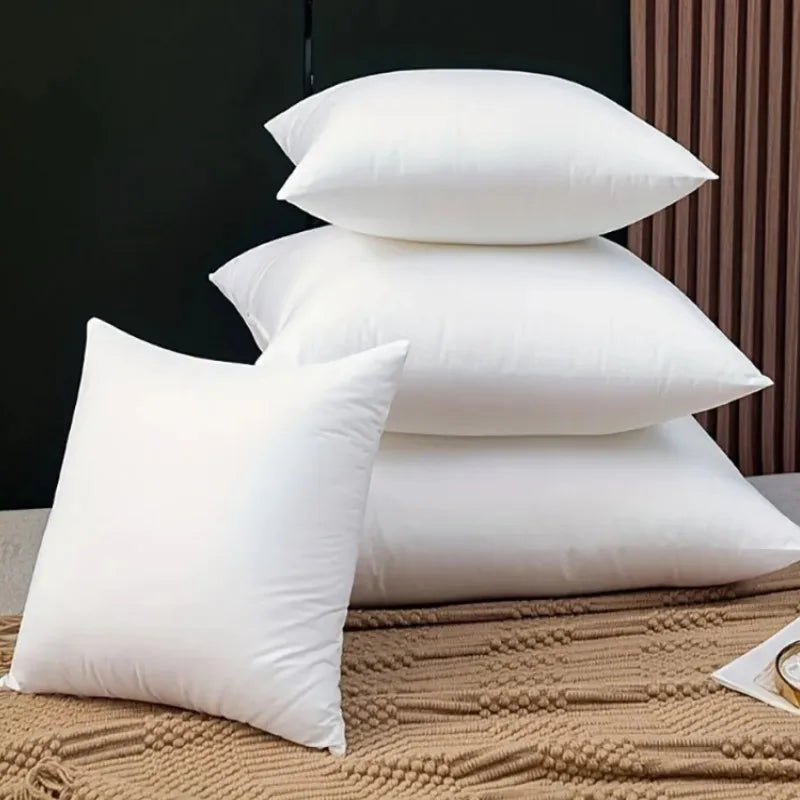 A stack of three white polyester cushion inserts for throw pillows resting on a beige fabric.