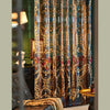 Long, sheer teal curtains with gold floral embroidery hang in a room next to a dark leather chair.