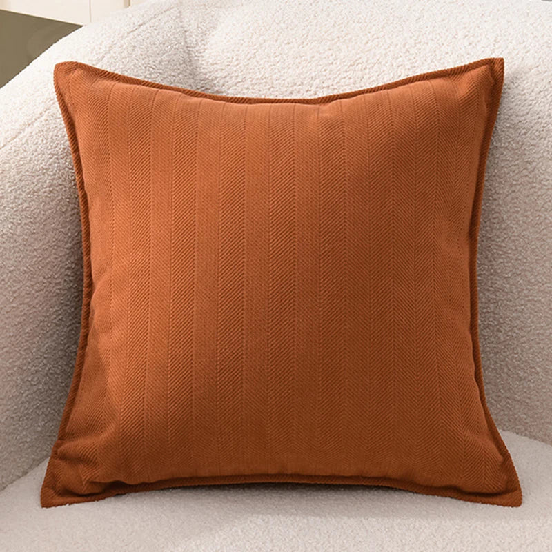 A square, textured rust-colored chenille throw pillow cover resting on a light-colored sofa.