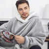 A man wearing a gray oversized flannel blanket is holding a dark-colored item.
