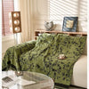A green chenille sofa slipcover draped over a light-colored sofa in a bright, sunlit room.