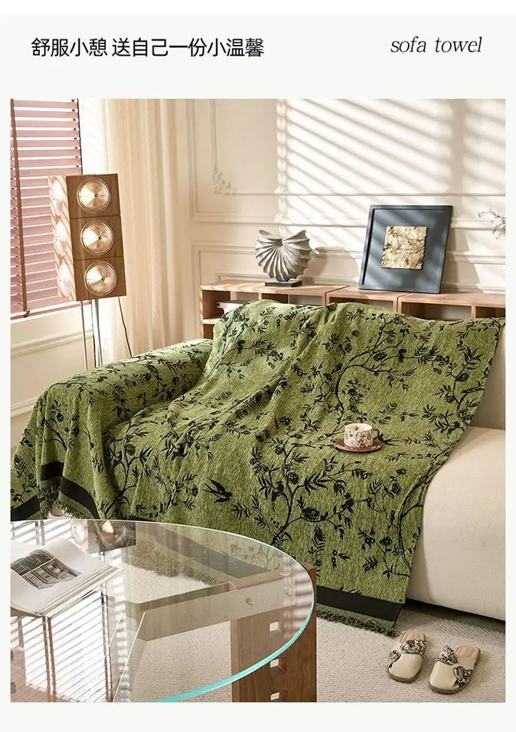 A green chenille sofa slipcover draped over a light-colored sofa in a bright, sunlit room.