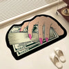 A hand is holding a stack of US dollar bills printed on an irregular black non-slip area rug.