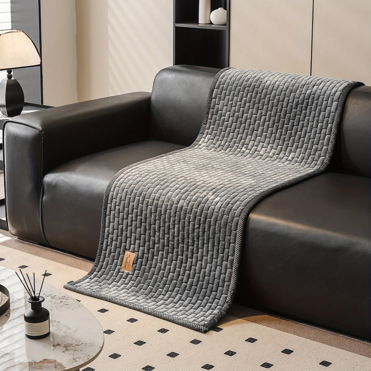 A gray quilted plush sofa cover draped over a dark leather sofa in a modern living room setting.