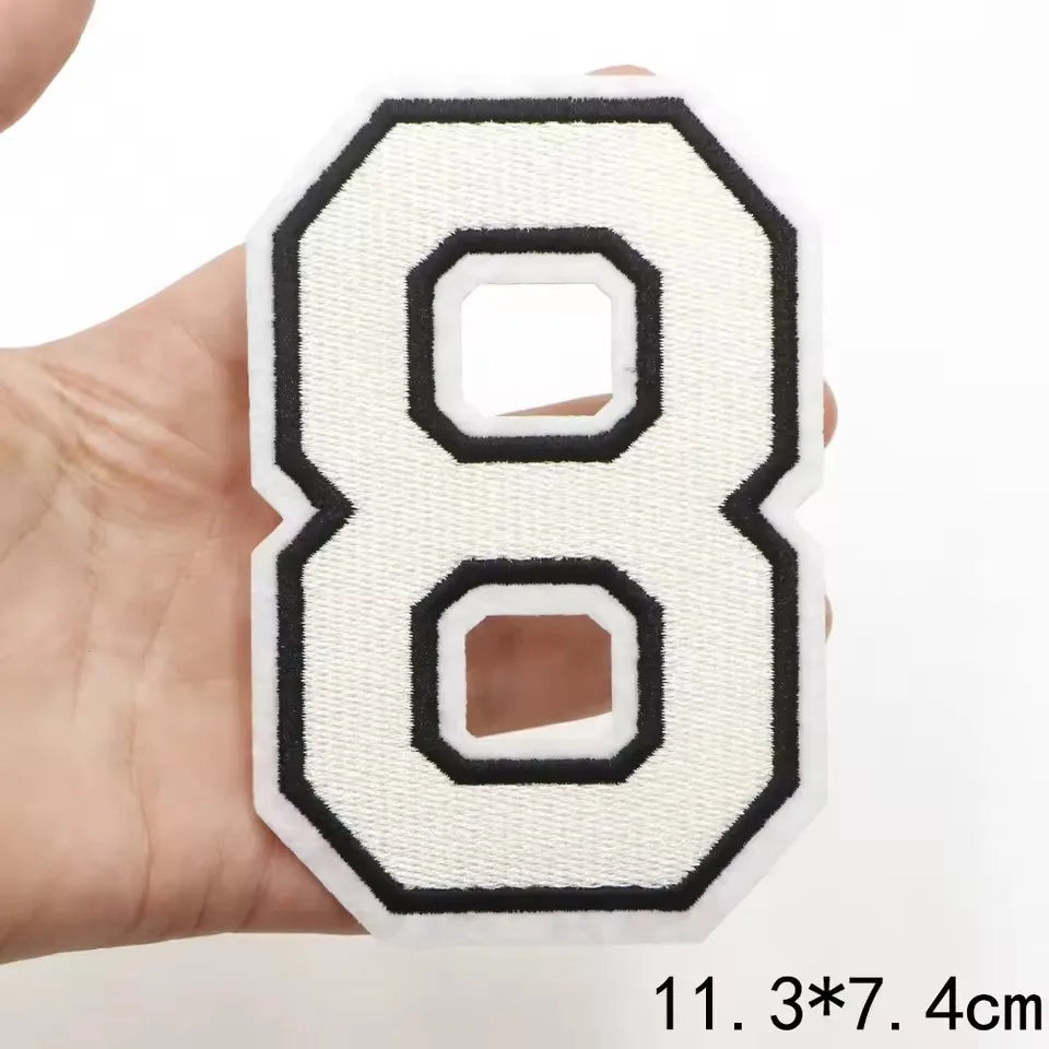 A white letter patch shaped like the number 8 with black outline and stitching, held in a hand.