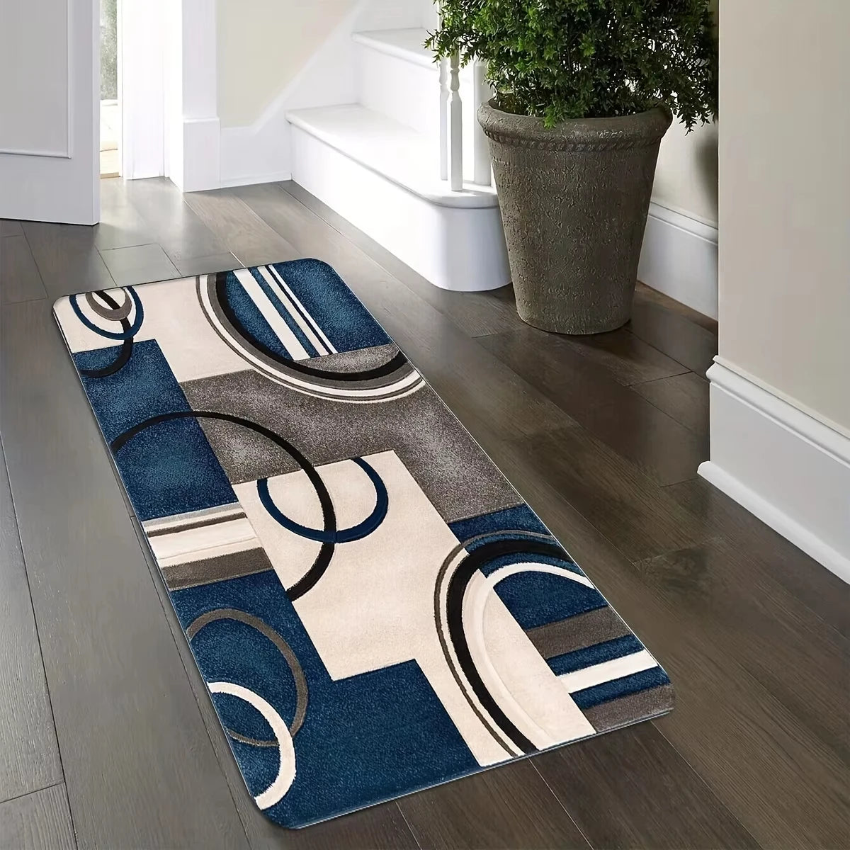 A rectangular geometric patchwork floor mat featuring navy blue, beige, and gray circular and rectangular patterns on a dark 