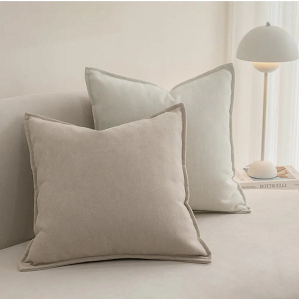 A beige solid chenille throw pillow cover resting on a light gray sofa next to a white lamp.
