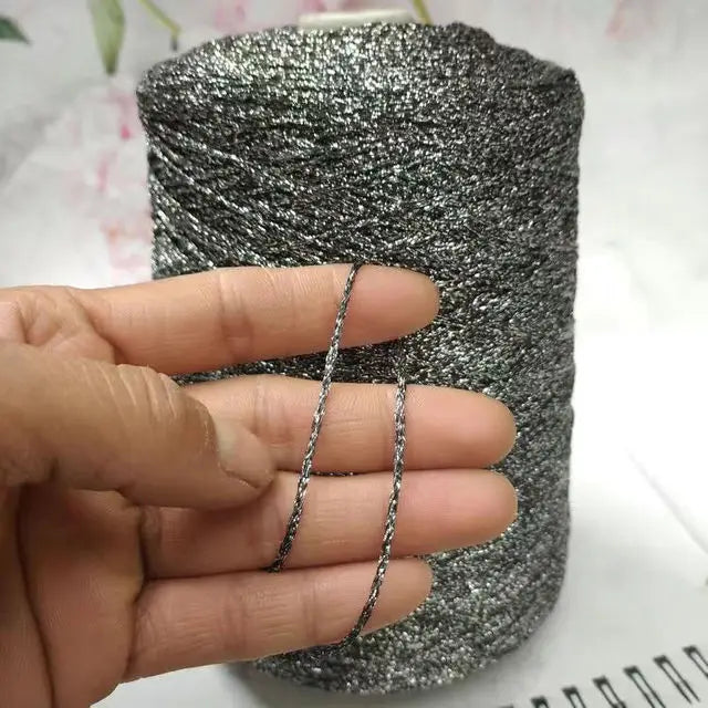 A hand holds a spool of silver glitter metallic yarn for crochet and knitting.