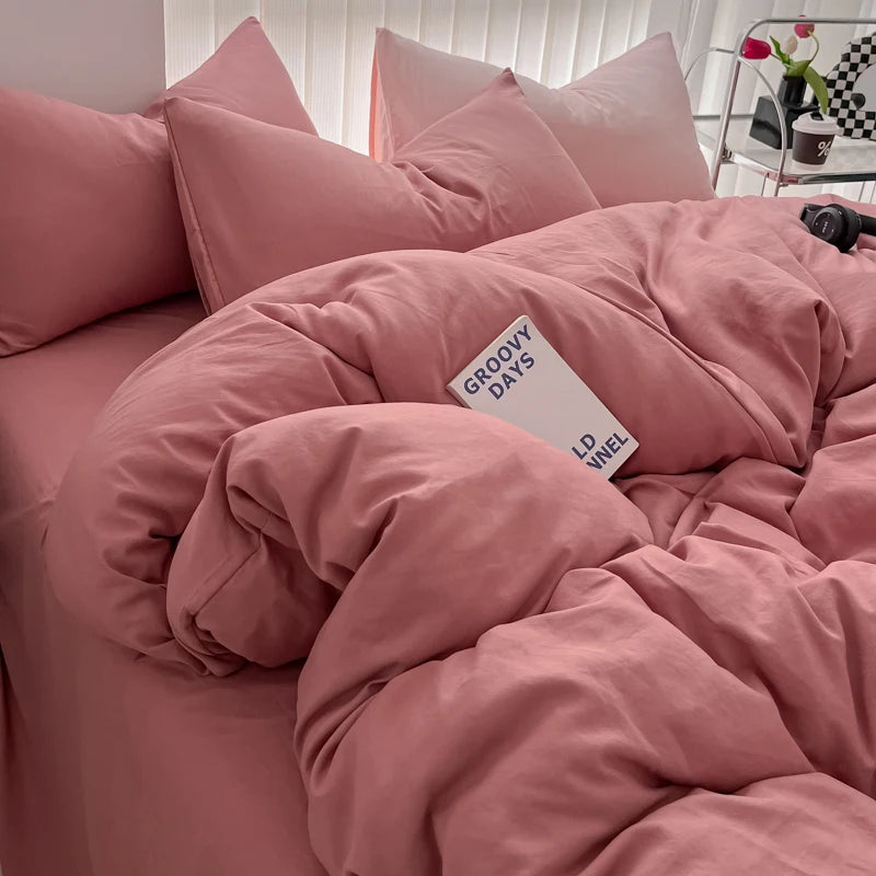 A pink duvet cover set with matching pillows and a folded pink blanket on a bed.