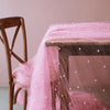 A pink pearl tulle table runner draped over a wooden table.