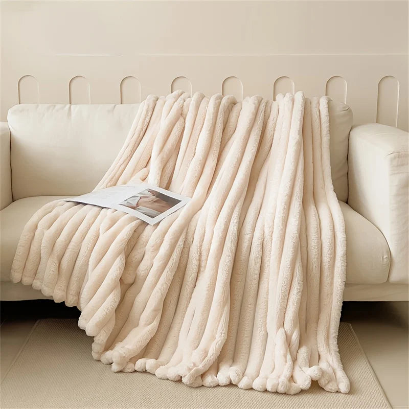 A thick, cream-colored fluffy blanket draped over a light-colored sofa.