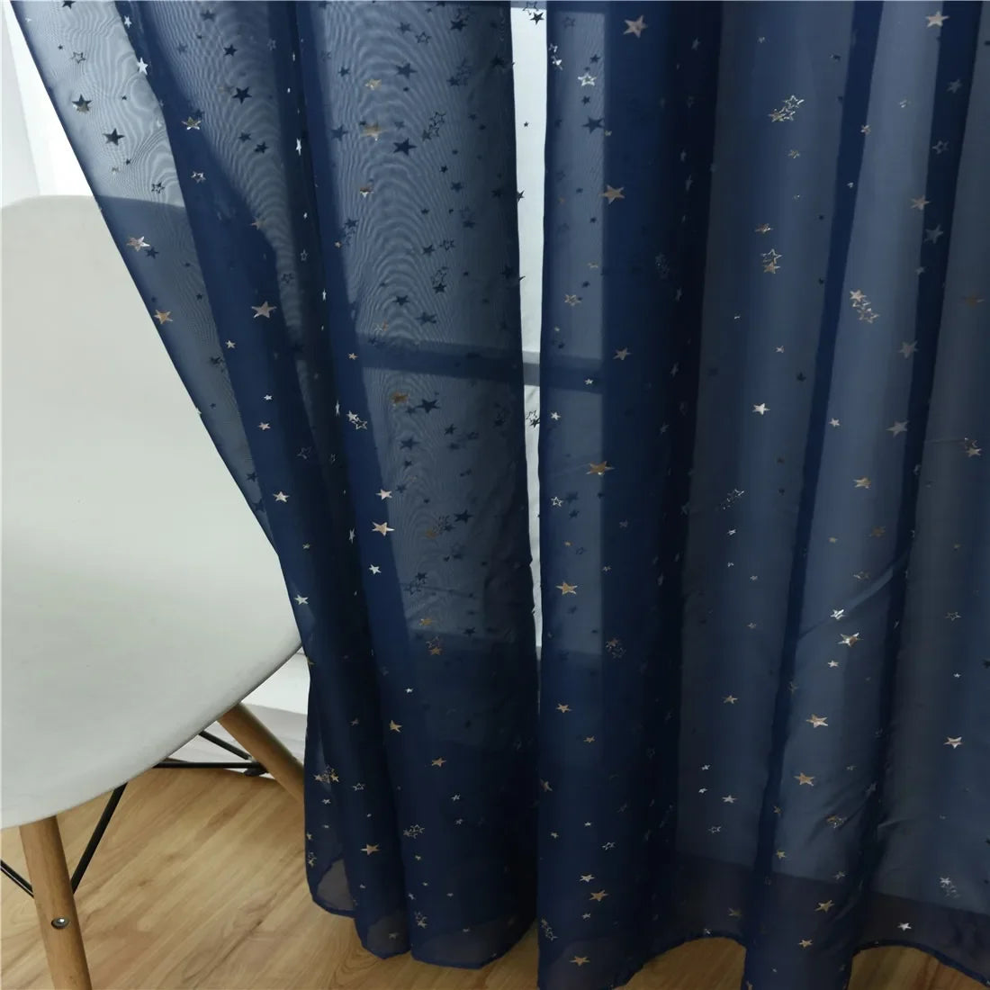 Dark blue tulle curtains decorated with small gold stars hanging next to a white table.