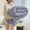 A person is holding a large, fluffy, lavender-gray plush winter blanket with white trim.