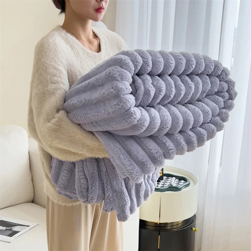 A person is holding a large, fluffy, lavender-gray plush winter blanket with white trim.