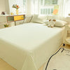 A white organic cotton bedding set with a quilted cover and a teddy bear pillow on a bed next to a window.