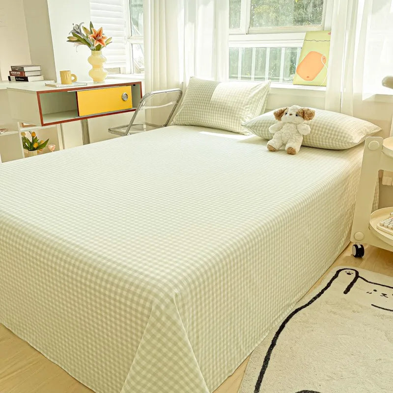A white organic cotton bedding set with a quilted cover and a teddy bear pillow on a bed next to a window.
