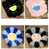Four variations of a cozy sunflower plush cushion with a smile face in black, pink, and blue colors.