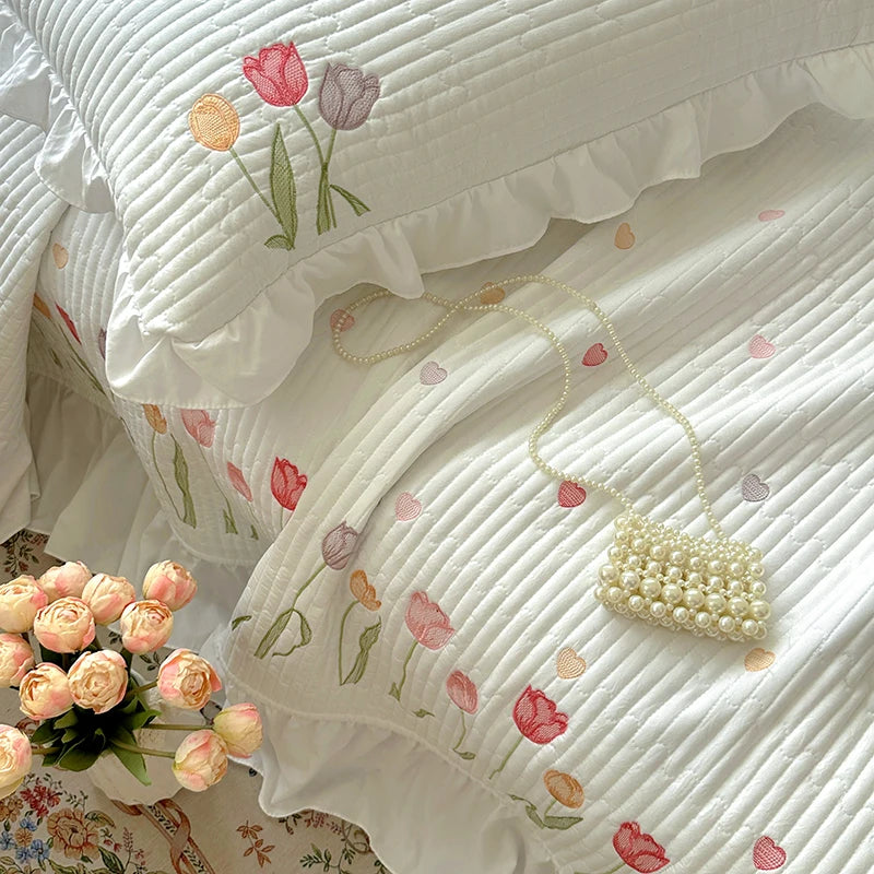 White quilted bedding set with pink and green floral embroidery and a pearl necklace