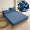 A folded blue fitted bed sheet set displayed on a wooden bed frame with a decorative throw pillow.