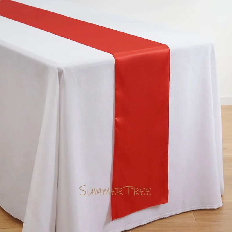 Elegant satin table runner in red and white draped over a white tablecloth.