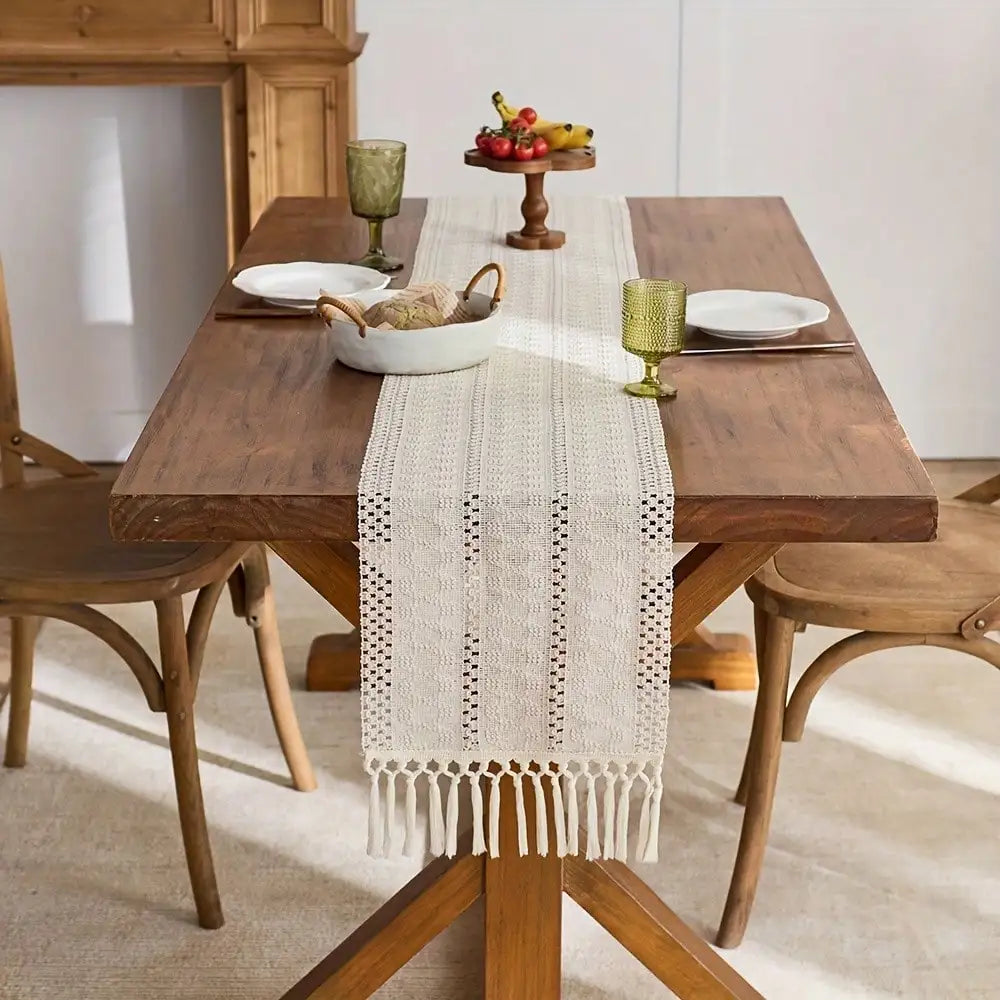 A wooden dining table set for a meal with a beige tasseled table runner and fruit