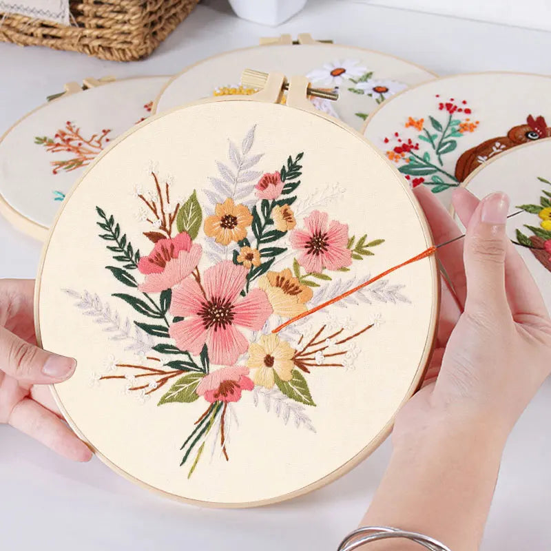 Hands are embroidering a floral pattern on a round canvas with a needle and thread.
