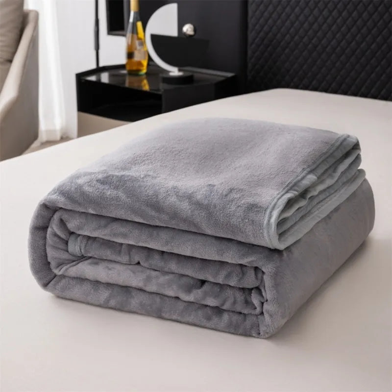 A stack of soft gray flannel throw blankets resting on a white surface.