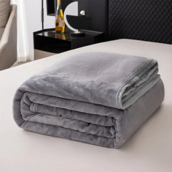 A stack of soft gray flannel throw blankets resting on a white surface.