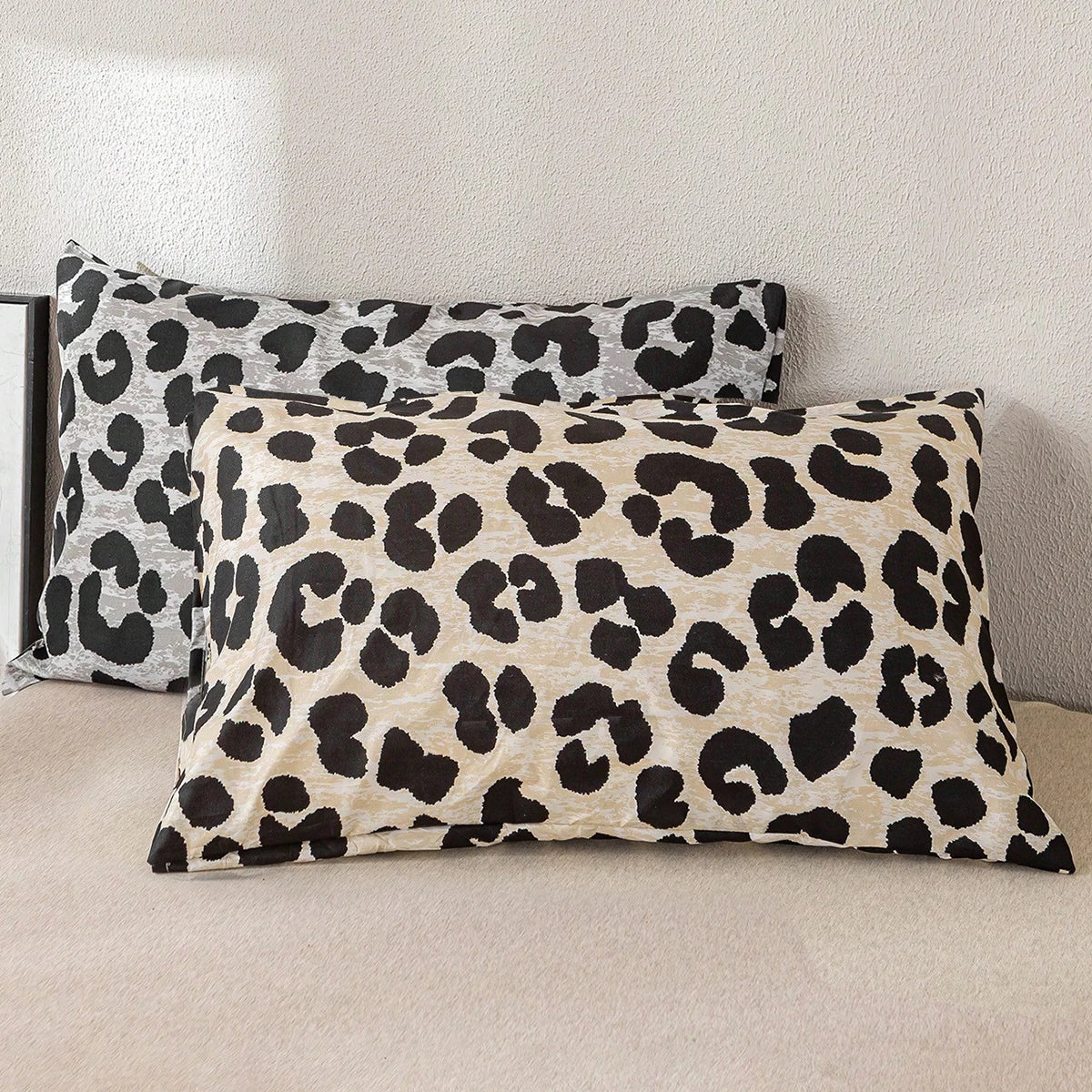 Two leopard print decorative pillow covers in black and beige are displayed on a light-colored sofa.
