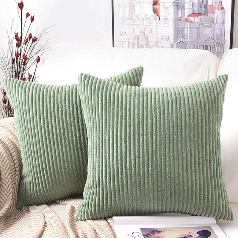 A close-up of a sage green corduroy striped throw pillow cover resting on a white sofa.