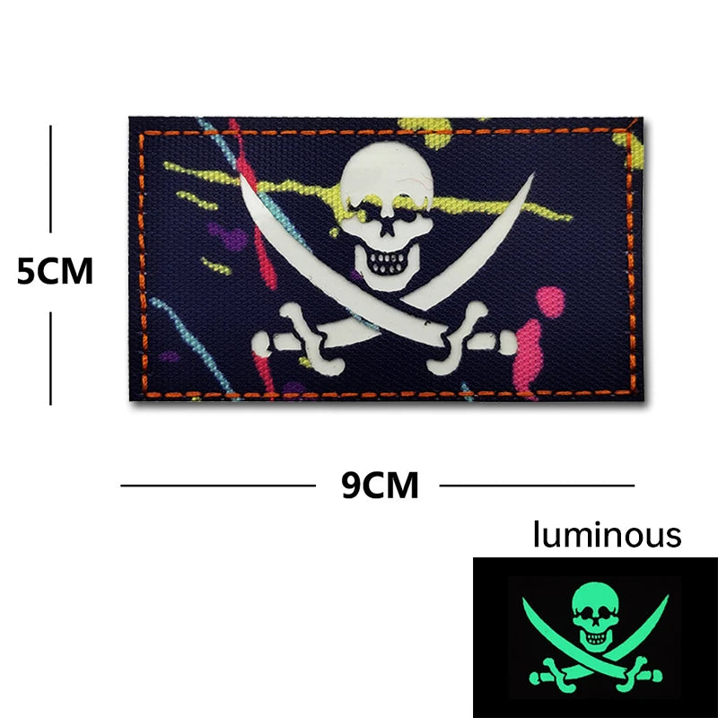 A dark blue embroidery patch featuring a white skull and crossed swords with colorful splatters on the fabric.