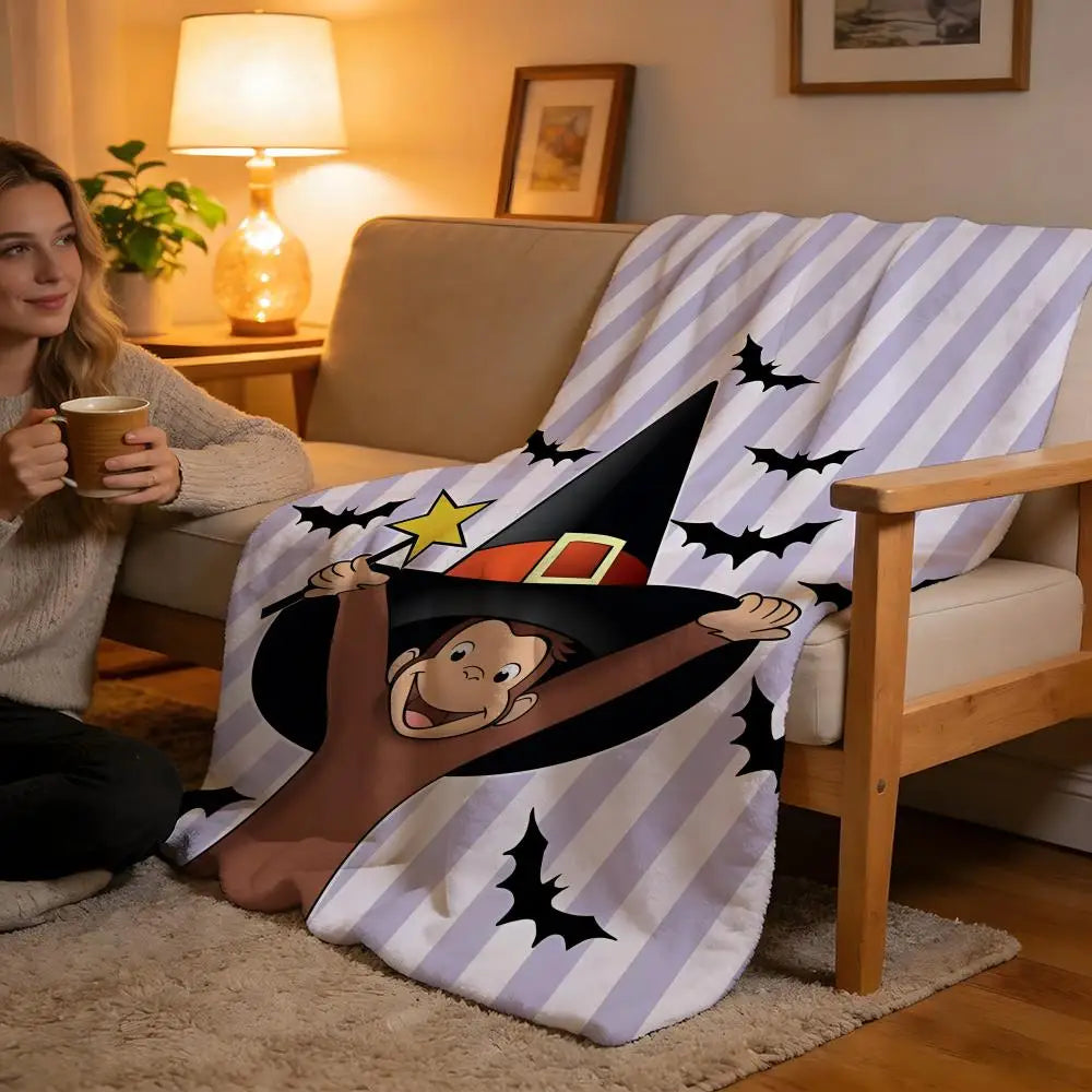 A person is sitting on a couch with a C-Curious George plush throw blanket featuring the character in a wizard hat design.