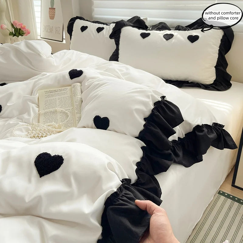 A close-up of a white duvet set with black embroidered hearts and ruffled fabric, featuring pillows and bedding.