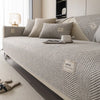 A light gray linen sofa cover with textured cushions and a matching throw blanket on a modern sofa.