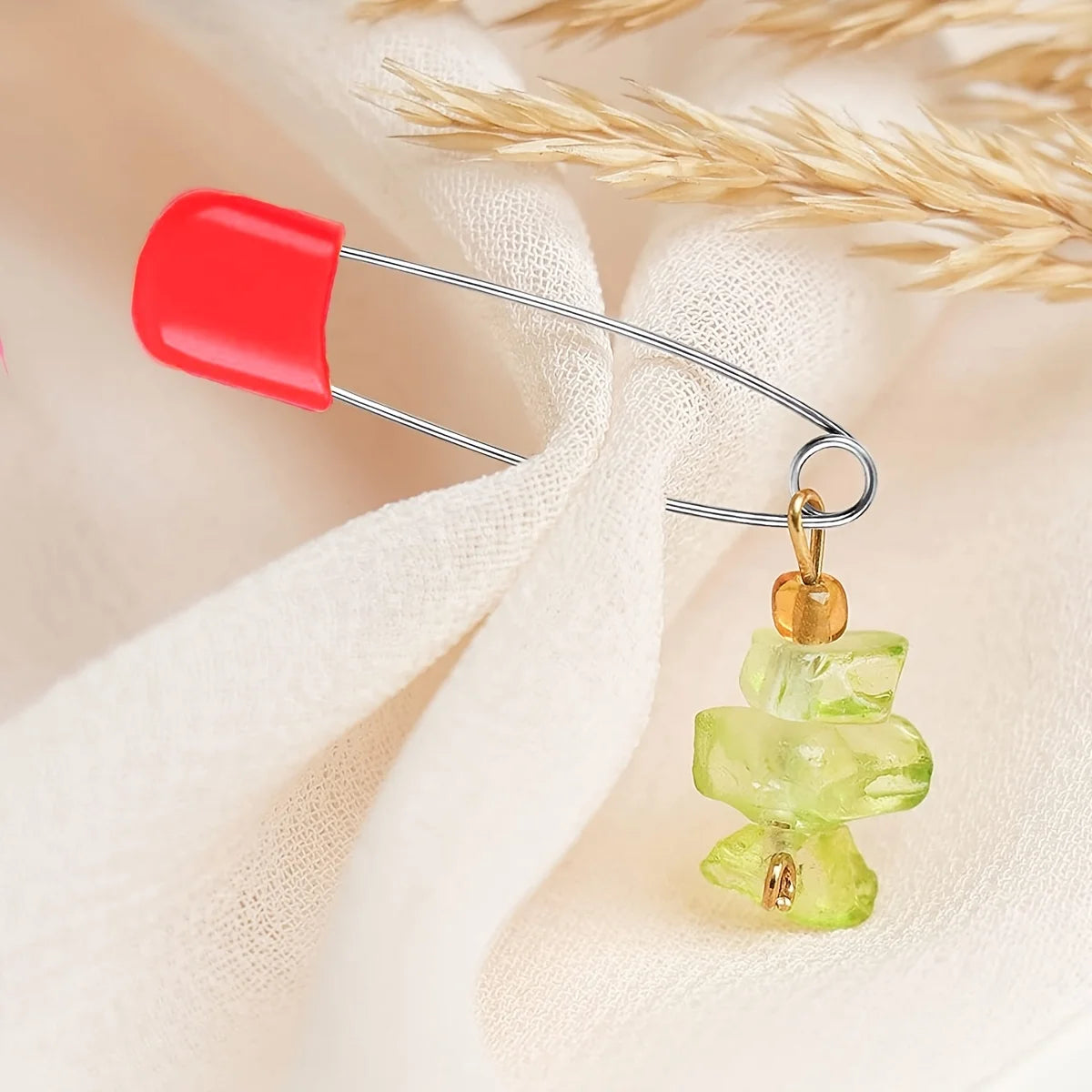 A red plastic safety locking closure diaper pin with a silver wire attached, displayed against a soft white fabric.