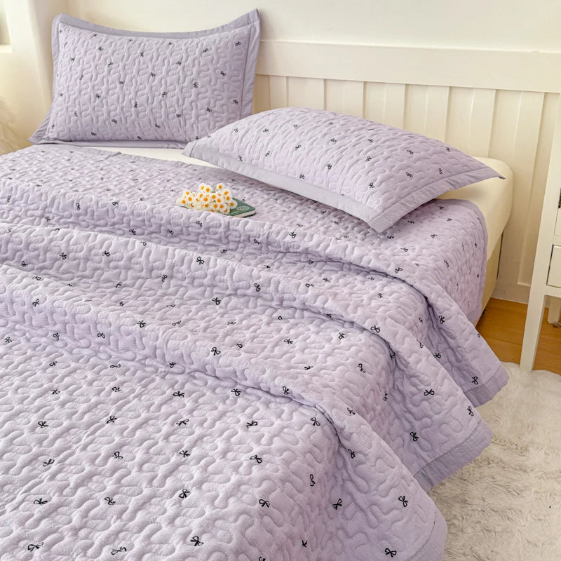 A purple floral quilted bedspread with small embroidered motifs is displayed on a bed.