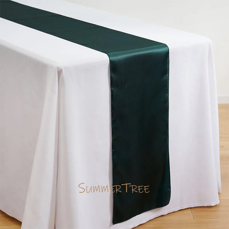 Elegant satin table runner in dark green laid across a white tablecloth.