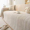 A beige sofa cover featuring an elegant fishbone pattern and a decorative pillow in a light neutral tone.