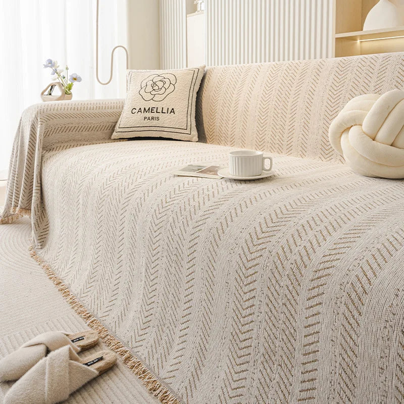 A beige sofa cover featuring an elegant fishbone pattern and a decorative pillow in a light neutral tone.