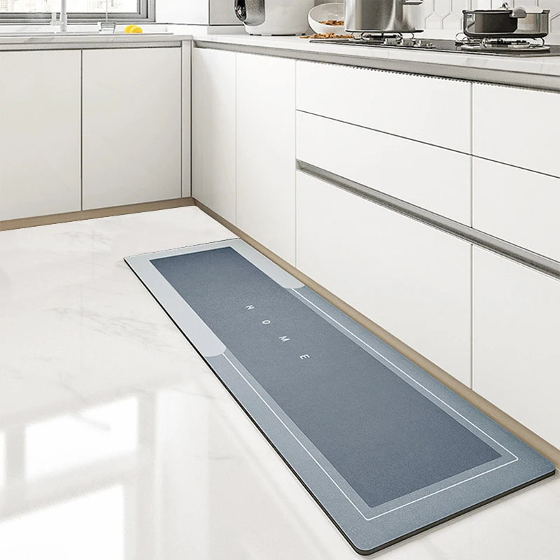 A rectangular gray non-slip floor mat with the word HOME printed on it placed on a white kitchen floor.