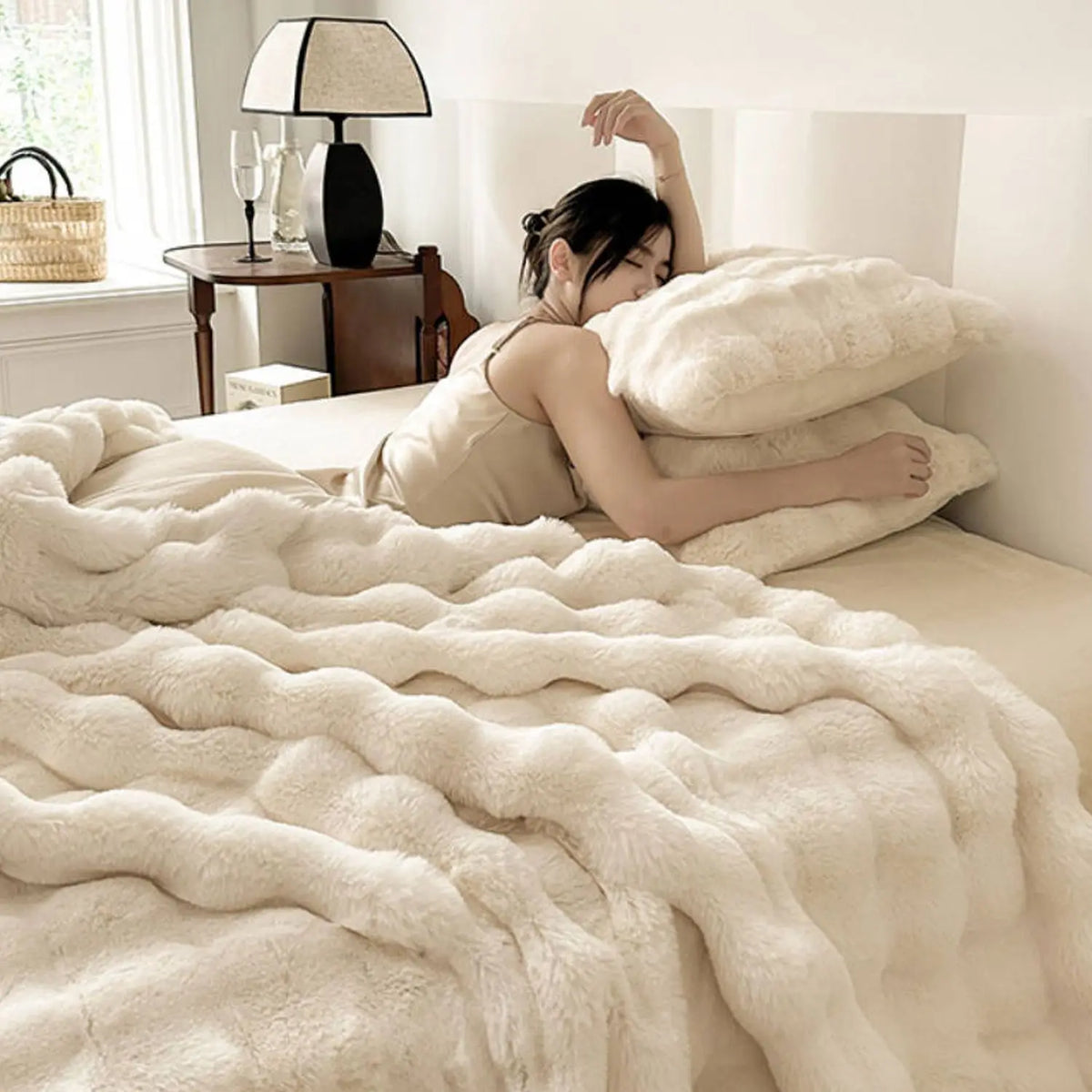 A woman lies on a bed covered with a plush faux rabbit fur throw blanket.