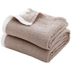 A stack of beige muslin throw blankets with white trim folded neatly.