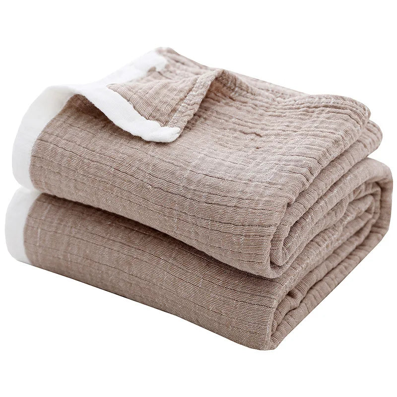 A stack of beige muslin throw blankets with white trim folded neatly.