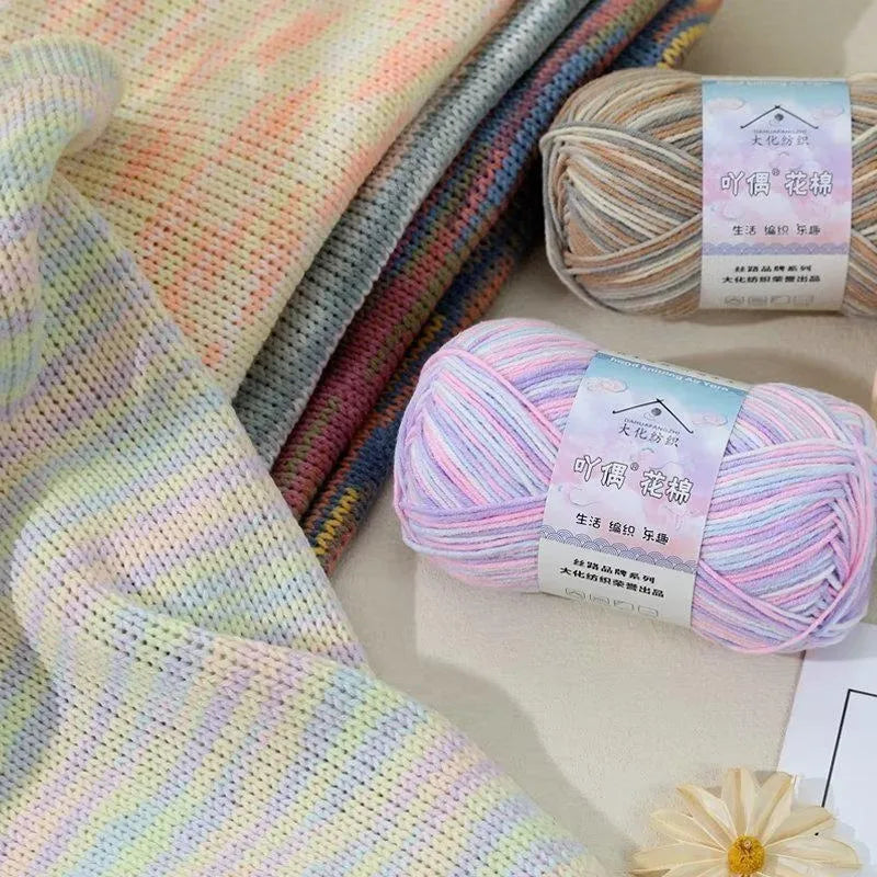 A bundle of multi-colored yarn in various shades of pink, purple, and white is displayed next to a finished knit fabric.